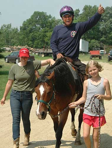 Ramiro Bermudez of Houston, Texas gives a thumbs-up while riding a horse at the National Wheelchair Sports Camp. Assisting Bermudez are Kate Kraus of Ironwood Springs Christian Ranch, left, and Maddie Harreld of Stewartville, a volunteer at Ironwood Springs.