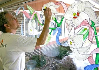 Tony Erickson of Stewartville, a landscape nurseryman who paints windows and murals, adds detail to the flowers he drew on a window near the entrance to the Stewartville Care Center on Friday, March 14. Erickson visited the Care Center regularly as a caregiver for Hal and Irene Giese before beginning a job as a nursing assistant there about a year ago. 