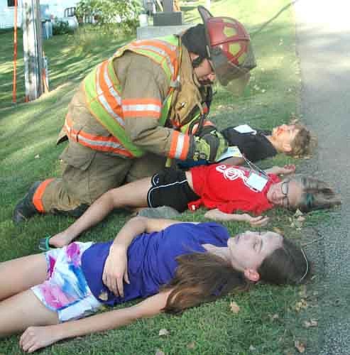 Josh Podein, a firefighter for the Stewartville Fire Department, tends to three students with simulated injuries at the site of a mock bus crash near the Stewartville Fire Station on Monday evening, July 31. The students include, from top to bottom, Gavin Clark, who will be a third grader at Bear Cave Intermediate School; Katy Struhar, who will be a fifth grader at Bear Cave School; and Alyssa Jones, who will be a freshman at Stewartville High School.