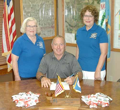 Mayor Jimmie-John King, seated in center, signs a proclamation declaring Sept. 8 and 9 Peanut Days in Stewartville. Janice Hagen, president of the Stewartville Kiwanis Club, standing at left, and Carol Youdas, club member, are two of the many club members who will accept donations to fight maternal and neonatal tetanus on those two days.