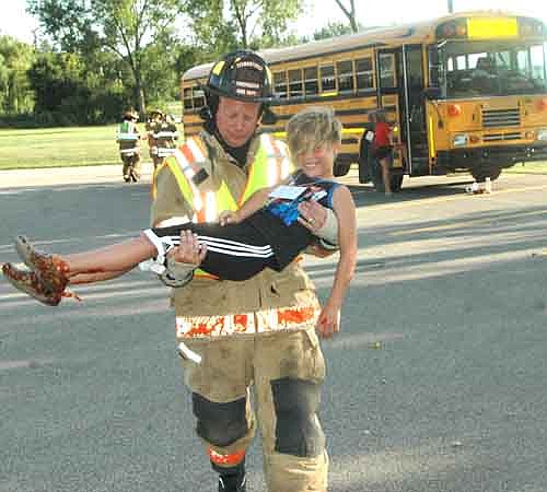 Aaron Jones, a firefighter for the Stewartville Fire Department, carries Patrick Olson to safety at the site of a mock bus crash near the Stewartville Fire Station on Monday evening, July 31. Patrick, "bleeding" ketchup from his ankles, is a fourth grader at Bear Cave Intermediate School.
