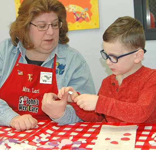 Lori Torgerson, the caterpillar teacher at St. John's Wee Care, left, helps Haddon Dagget, 4, decorate a bag with valentine hearts on Valentine's Day morning, Wednesday, Feb. 14.