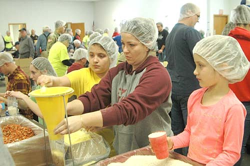 Jacqui Rinn of Stewartville holds a plastic bag under a funnel as her daughter Riley, 11, left, adds an ingredient and daughter Reese, 7, right, waits to add another during the 15th annual Food for Kidz food-packaging event for the poor at the Stewartville Civic Center.