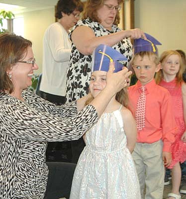 Dee Radtke, director of St. John's Wee Care, adjusts the cap of graduate Bree Lawson at the annual Wee Care graduation at St. John's Lutheran Church on Sunday, May 6. In back, center, Lori Torgerson, caterpillar and butterfly teacher at Wee Care, places a cap on the head of graduate James Meyer. In back at far left, Becky Case, a caterpillar aide, prepares to assist graduate Amy Rentz, in back at far right.