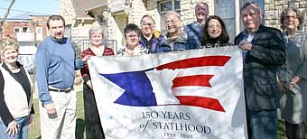 UNFURLING THE BANNER -- A banner commemorating the state of Minnesota's 150th year of statehood arrived in Stewartville last week, courtesy of  Chatfield mayor Curt Sorenson,  standing second from left, who brought the banner from his city.  Stewartville city officials who celebrated the occasion include, front row, from left, Cheryl Roeder, Barb Neubauer, Deb Lofgren, Don "Buck" Amos, Pat Johnson, director of the Stewartville Public Library, and Mayor Chuck Murphy. Standing in back, from left, Dick Uptagrafft, Bill Schimmel Jr., city administrator; and Ann Hutton of SELCO.  