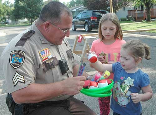 Sixteen Stewartville homes hosted registered gatherings to celebrate National Night Out on a beautiful Tuesday evening, Aug. 7 last week. Above, Sgt. Kirby Long of the Olmsted County Sheriff's Office, a former community oriented policing (COPS) deputy in Stewartville, offers a variety of toys to two young ladies at an NNO&#8200;celebration hosted by Jenny Anderson at the 400 block of Fourth Avenue Southeast. Arianna McCrossen, 3, of Stewartville, selects a ball as Brystol Schmidt, 8, of Stewartville waits her turn in the background.