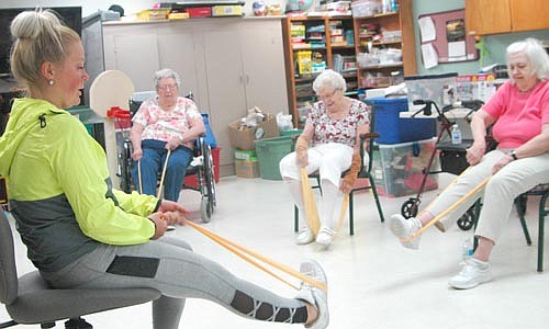 Lex Robertson, strength and conditioning coach and personal trainer at Anytime Fitness of Stewartville, left, demonstrates how to use a TheraBand during a workout at the Stewartville Care Center on Thursday morning, Aug. 9. From left in the background are Care Center residents Mary Kuisle, Evelyn Galligos and Carol Kelly.
