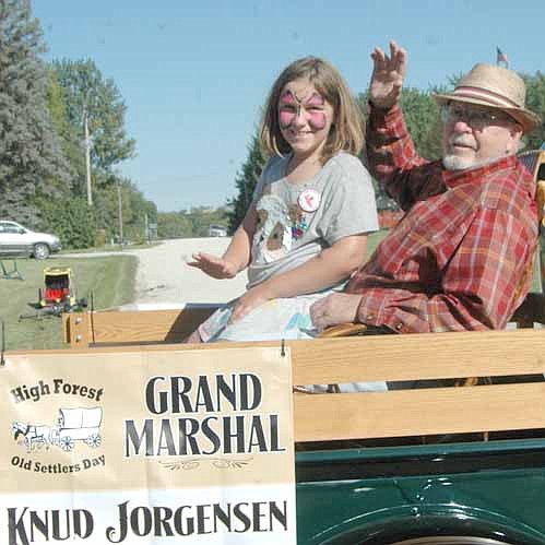 Knud Jorgensen, grand marshal of this year's Old Settlers Day Parade, waves to the audience along the parade route. Grace Amy, a fourth grader at Bear Cave Intermediate School and Jorgensen's granddaughter, rides along with her grandpa.