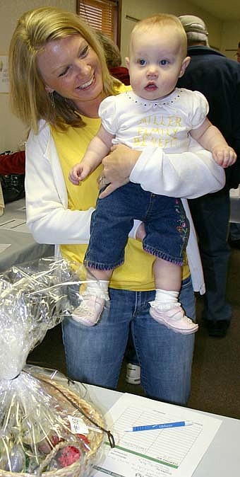 Crisha Miller of Solon, Iowa, above, holds her 9-month-old daughter Mya as she reviews auction items at the Miller benefit on Saturday, April 19. 
