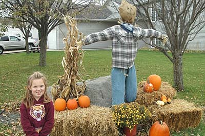 Kendall Ryan, 5, a kindergartner at Bonner Elementary School, poses near her family's fall decoration along Countryview Court Southeast. "The whole family did  the scarecrow and I did the pumpkins with the stickers on it," she said. She said she enjoys Halloween, especially going trick-or-treating.
