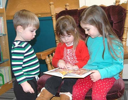 Grace Koza, 3, of Stewartville, wearing the read sweater, points to something interesting as she reviews a book a few minutes before story time began at the Stewartville Public Library on Tuesday, Dec. 11. Looking on, from left, are Jack Angeli, 2, of Rochester, and Jack's sister Alice Angeli, 4.